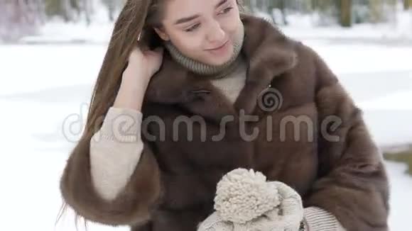 冬天穿着毛茸茸外套在公园里摆姿势的漂亮女孩慢慢地视频的预览图