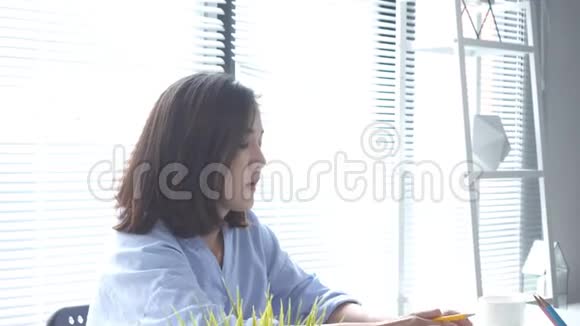美丽的年轻拉斯特亚裔妇女在家里坐在客厅里用笔记本电脑工作视频的预览图