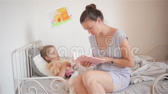 年轻的妈妈给孩子读床上的故事妈妈让女儿睡觉视频的预览图