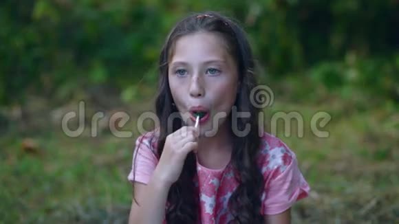 漂亮的小女孩在花园里吃棒棒糖视频的预览图