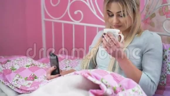 金发美女躺在床上在4K里喝酒和使用手机视频的预览图