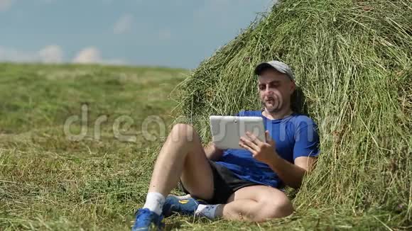 穿着深蓝色t恤的人坐在干草堆附近通过平板电脑进行交流视频的预览图