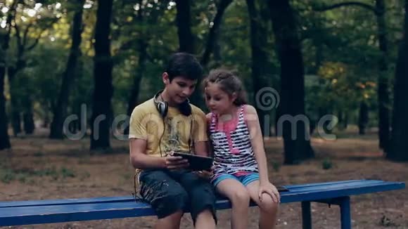 儿童平板电脑户外在草地上玩电脑的女孩和男孩视频的预览图