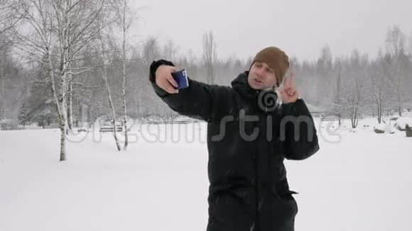 人在白雪皑皑的冬林里制作自拍手机他微笑着改变姿势以获得更好的照片可用性视频的预览图