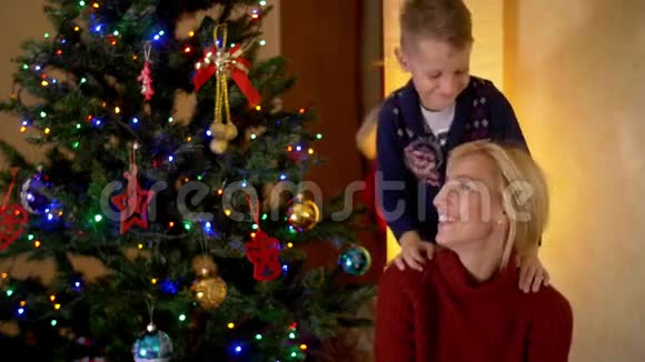 快乐的金发母亲和她的儿子在圣诞树下视频的预览图