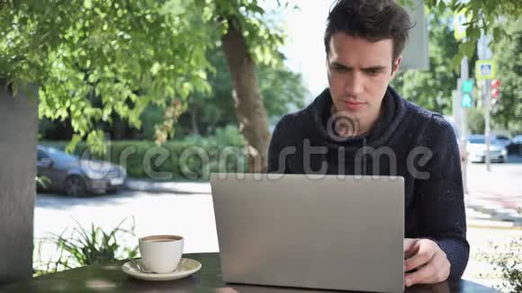 年轻人坐在咖啡馆的露台上打手提电脑视频的预览图