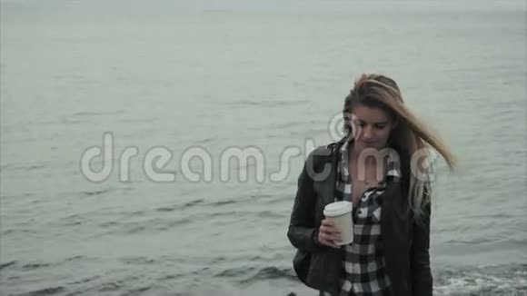 迷人的金发女郎手里拿着一杯咖啡靠近大海视频的预览图