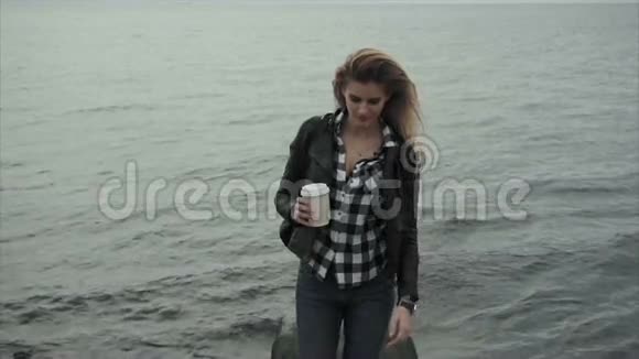 可爱的金发女郎手里拿着一杯咖啡靠近大海视频的预览图