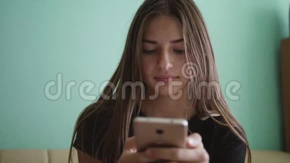 漂亮的金发白种人少女坐在家里的沙发上发短信微笑着笑着的女人爱情视频的预览图