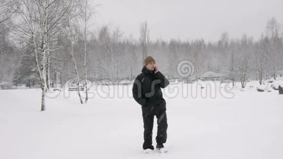 一个年轻人在冬天的森林里打电话大雪纷飞他停下来结束了谈话一个男人视频的预览图