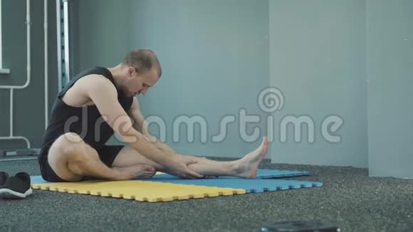 在蓝色黄色垫子上做伸展运动和热身运动时男人看起来很严肃视频的预览图