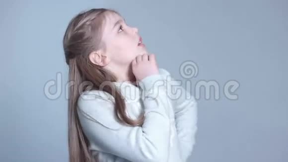 可爱的小女孩在灰色背景下思考的特写肖像视频的预览图