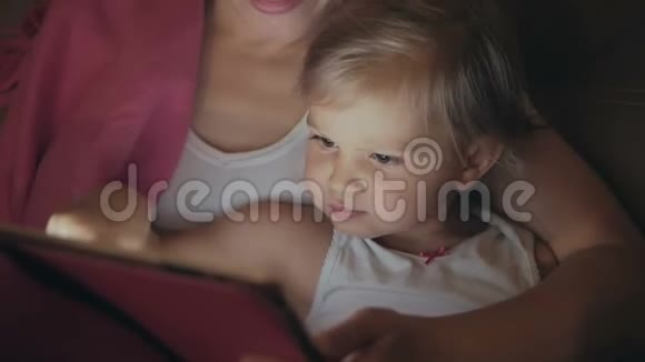 妈妈和一个小女儿躺在床上看着电子平板电脑的屏幕视频的预览图