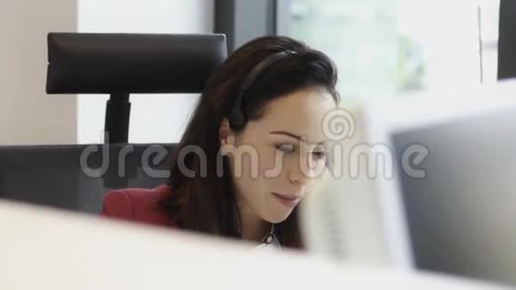 美丽的年轻女子在办公室呼叫中心的耳机上交谈视频的预览图