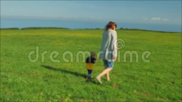 年轻的妈妈和她美丽的儿子在阳光明媚的日子在绿茵场上散步视频的预览图