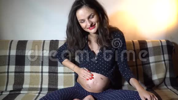 幸福的孕妇躺在沙发上抚摸她的肚子视频的预览图
