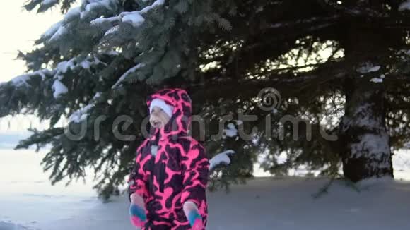 一个穿着连衣裙的快乐孩子玩着降雪树慢动作视频的预览图
