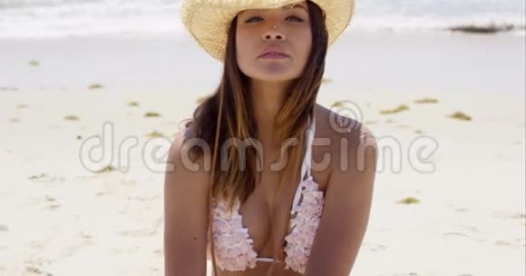 美丽的年轻女子坐在沙滩上的草帽里视频的预览图