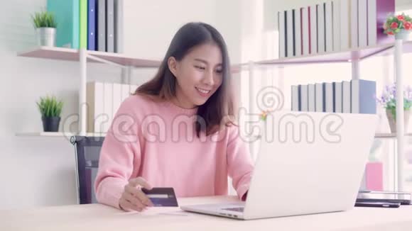 美丽的亚洲女人用电脑或笔记本电脑通过信用卡购买网上购物视频的预览图