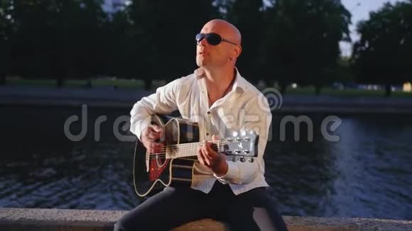 人弹吉他对着湖面唱歌吉他手触摸吉他弦中弹视频的预览图