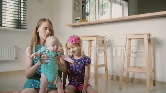 漂亮的年轻妈妈和她的小儿子和可爱的小女儿坐在厨房的地板上慢动作视频的预览图