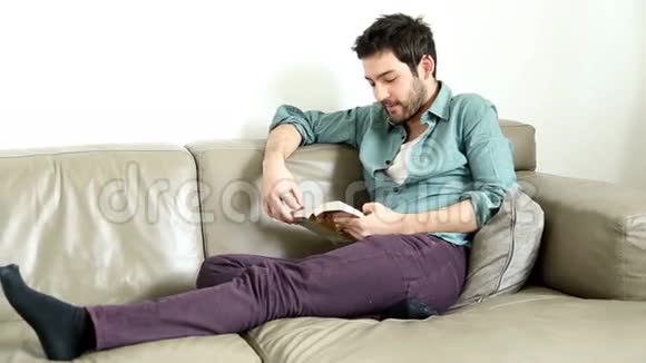可爱的男人坐在沙发上看书微笑着视频的预览图