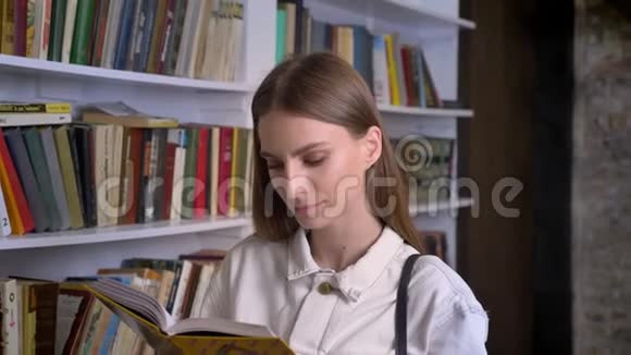 年轻可爱的女孩正在看书在镜头前看在后台看图书馆视频的预览图