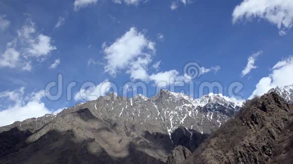 轻盈的白云衬着一片蓝天漂浮在高高的崎岖的山脉上有雪的残余高加索格鲁吉亚视频的预览图