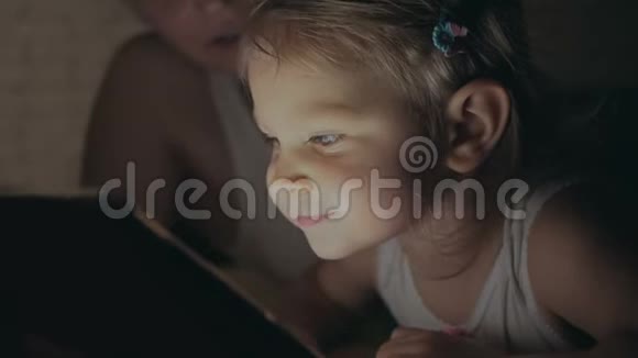妈妈和一个小女儿躺在床上看着电子平板电脑的屏幕视频的预览图