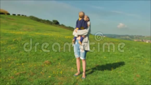 年轻的妈妈和她美丽的儿子在阳光明媚的日子在绿茵场上散步视频的预览图