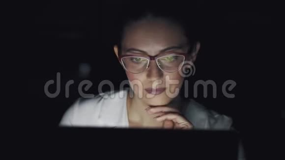 一个商务女性在笔记本电脑上工作到很晚的肖像带眼镜的屏幕反光视频的预览图