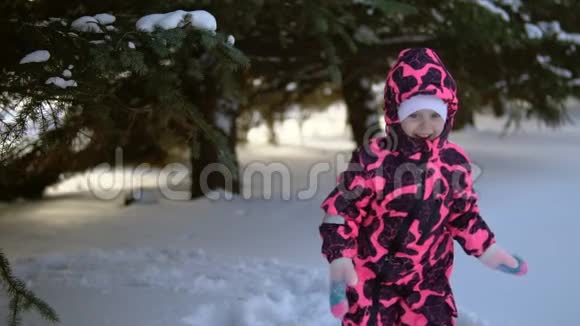 一个穿着连衣裙的快乐孩子玩着降雪树慢动作视频的预览图
