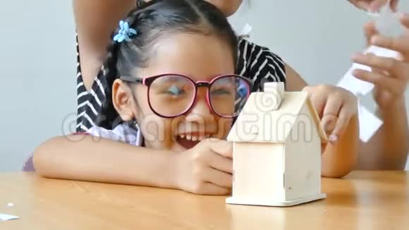 穿着泰国幼儿园学生制服的近镜头亚洲小女孩和她的母亲在玩一张白纸做成家庭形状视频的预览图