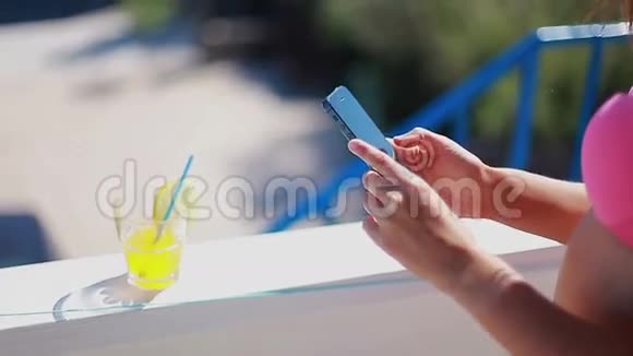 穿粉色泳衣的女孩在智能手机上拍摄柠檬鸡尾酒视频的预览图