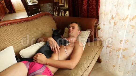 一天中睡在沙发上的人拿着电话里的耳机4k慢动作黑猫躺在视频的预览图