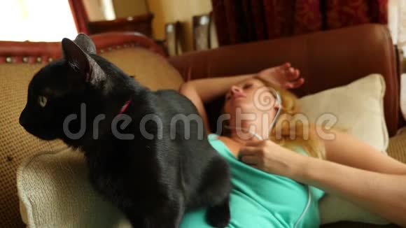 一天中睡在沙发上的人拿着电话里的耳机4k慢动作黑猫躺在视频的预览图