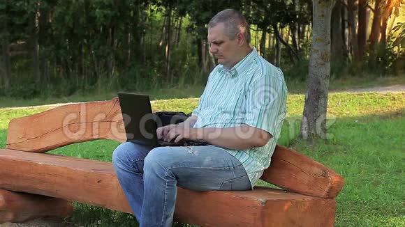 坐在长凳上的人在公园里用笔记本电脑视频的预览图