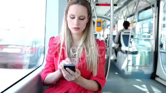 年轻的金发女子骑着电车在手机手机手机上打字视频的预览图