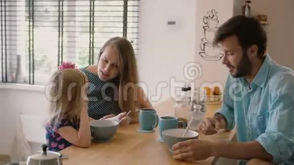 年轻的父母早上和他们的小女儿在厨房的餐桌上吃早餐斯泰迪卡姆慢镜头视频的预览图
