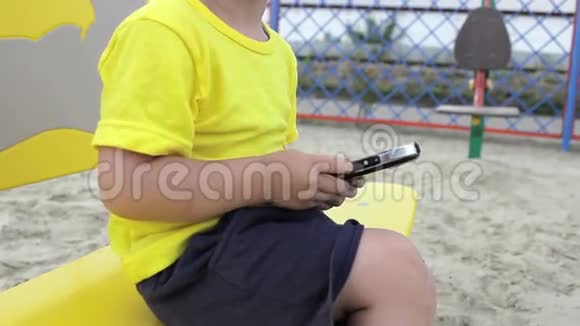 一个小男孩坐在长凳上玩电话视频的预览图
