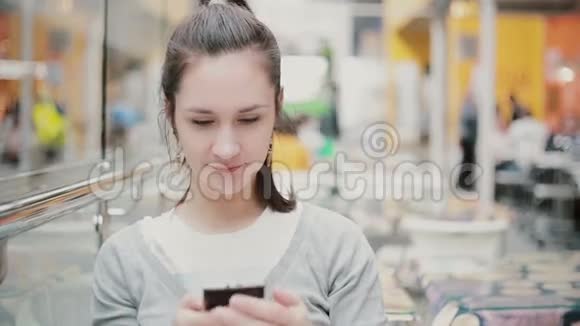 一个年轻的女人坐在公共场所用她的电话微笑视频的预览图