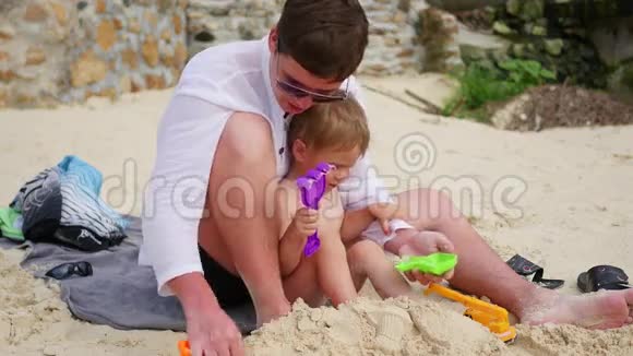 一个年轻人在海滩上和孩子玩做沙子的模子视频的预览图