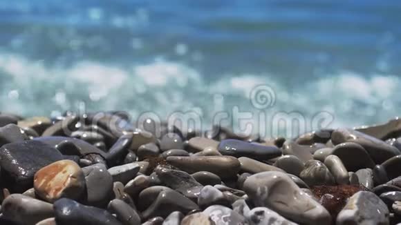 海上冲浪者正在飞溅卵石海滩波浪在多种颜色的抛光石和卵石上移动近距离观看慢慢慢慢视频的预览图