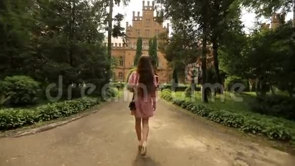 在古老的大学建筑周围的旧公园里的艾莱里年轻女子的后拍视频的预览图