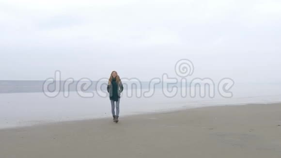 在沙滩上走向镜头在雾霭中微笑的年轻漂亮女孩视频的预览图