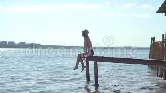 女人坐在木码头边上放松双腿在水面附近摆动视频的预览图