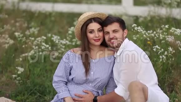 未来的爸爸妈妈坐在田里有丈夫的孕妇把手放在肚子上视频的预览图