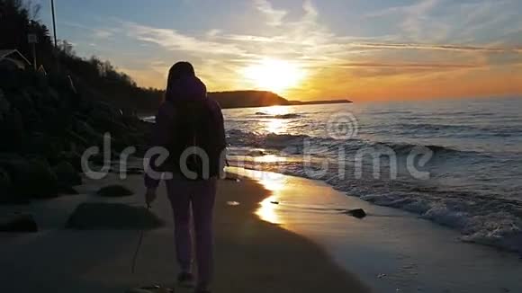 美丽的年轻女孩在阳光的背景下沿着海滩散步粉红色的衣服春天慢动作视频的预览图