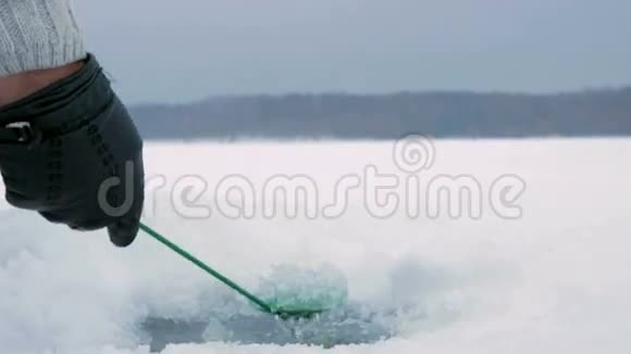 这个人正在冰冻的湖面上从事冬季捕鱼活动清除冰壳上的洞视频的预览图