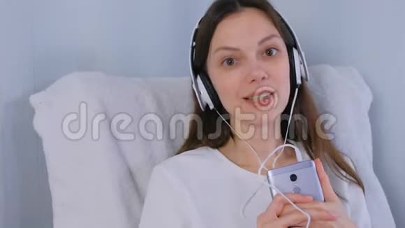 女人在智能手机上用耳机听音乐唱一首歌视频的预览图